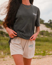 Person wearing a dark gray t-shirt and beige shorts with visible branding outdoors.