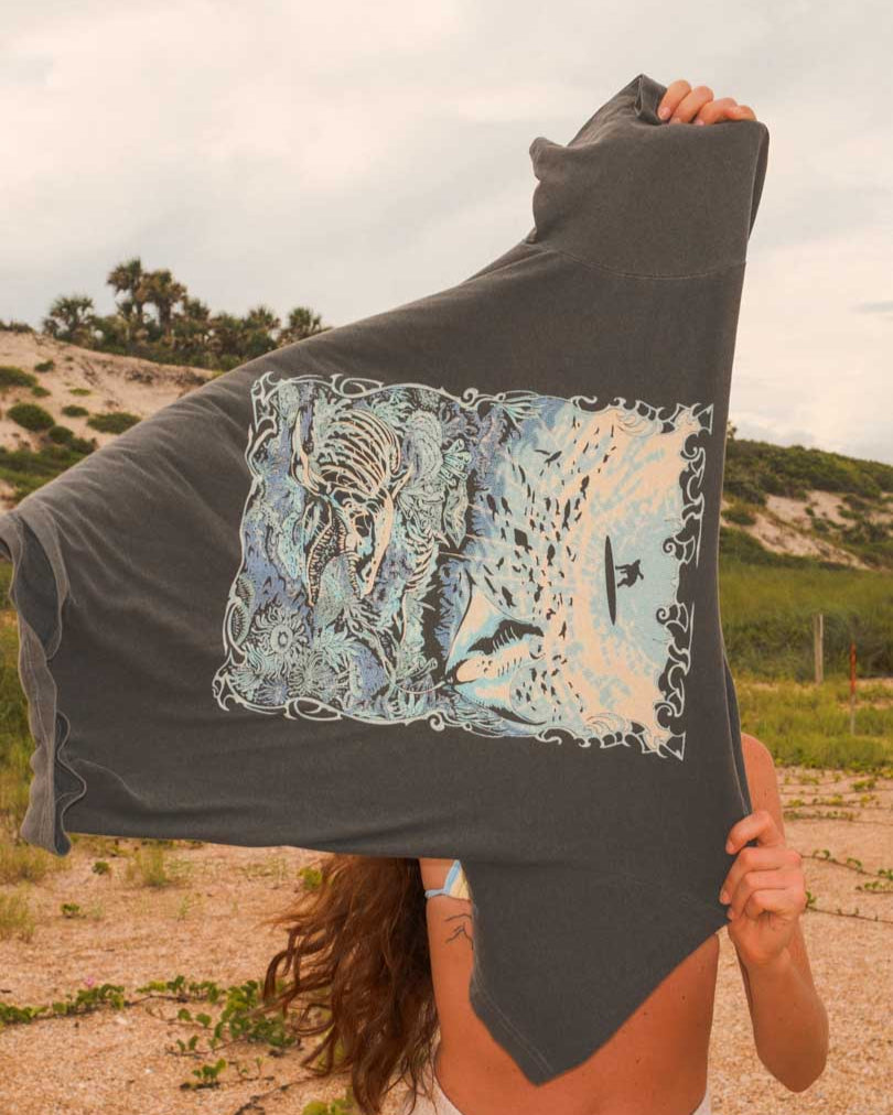 Person holding a dark gray tshirt with a colorful graphic design outdoors.