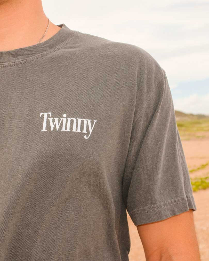 Person wearing a gray t-shirt with 'Twinny' logo outdoors