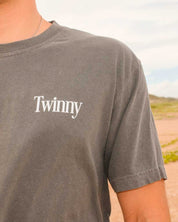 Person wearing a gray t-shirt with 'Twinny' logo outdoors